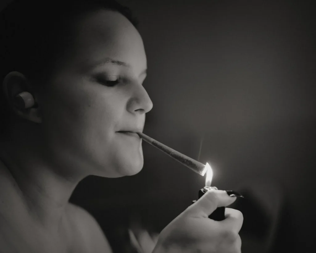 Black-and-white candid portrait of a person lighting a smoke in a quiet low-light moment