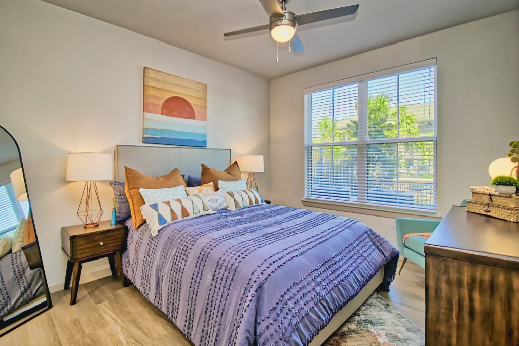 Interior photo of a styled bedroom with purple bedding and natural window light