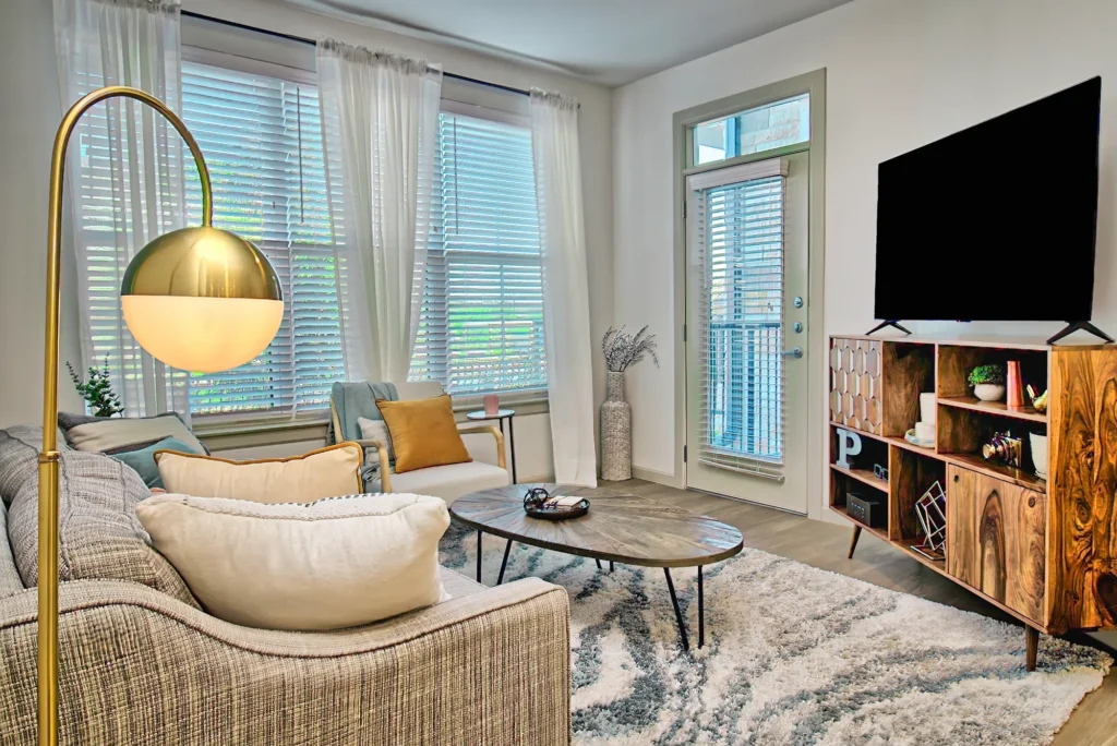 Warm interior photo of a living room with a gold floor lamp, large windows, and textured decor